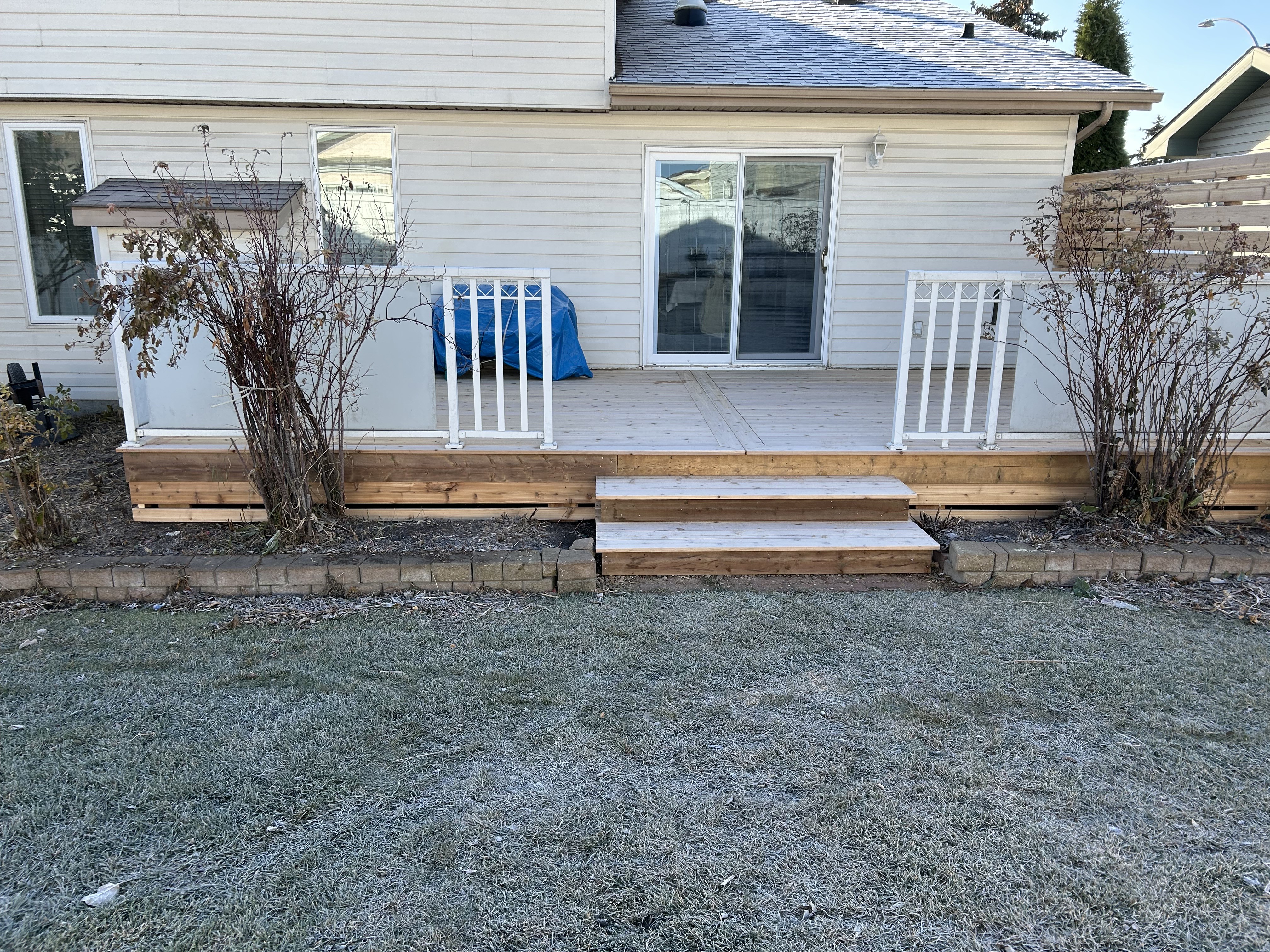 New cedar deck with elegant picture frame design, white railings, and wide steps leading to backyard in Edmonton home